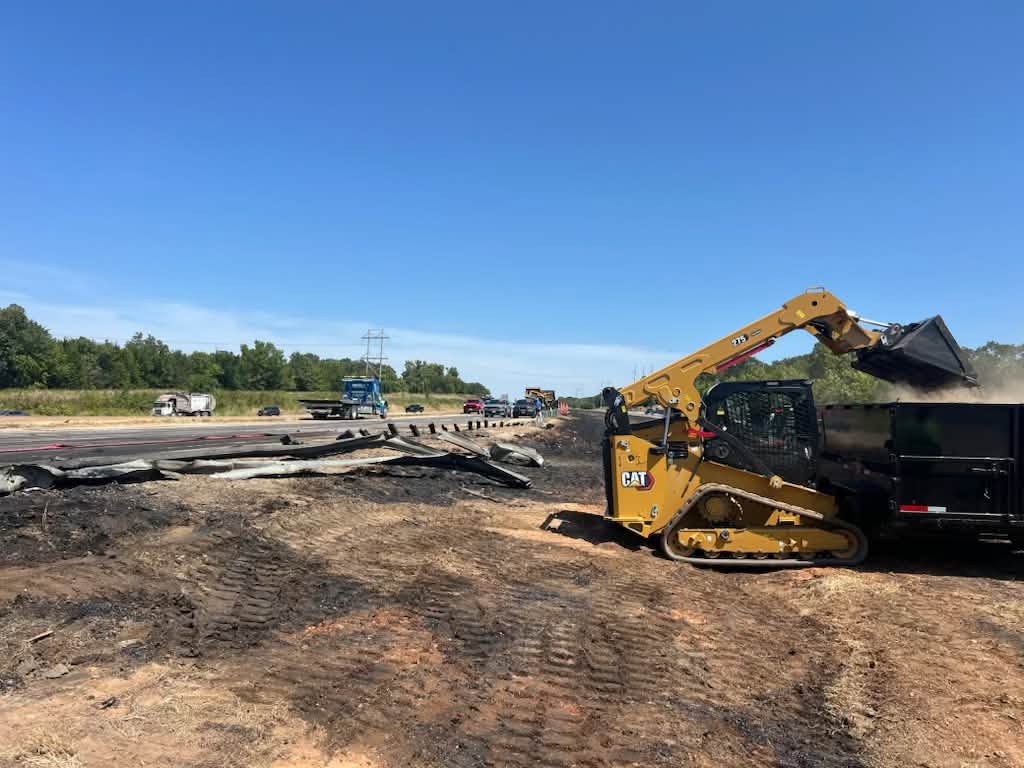 Skid steer clearing the spilled load beside the highway