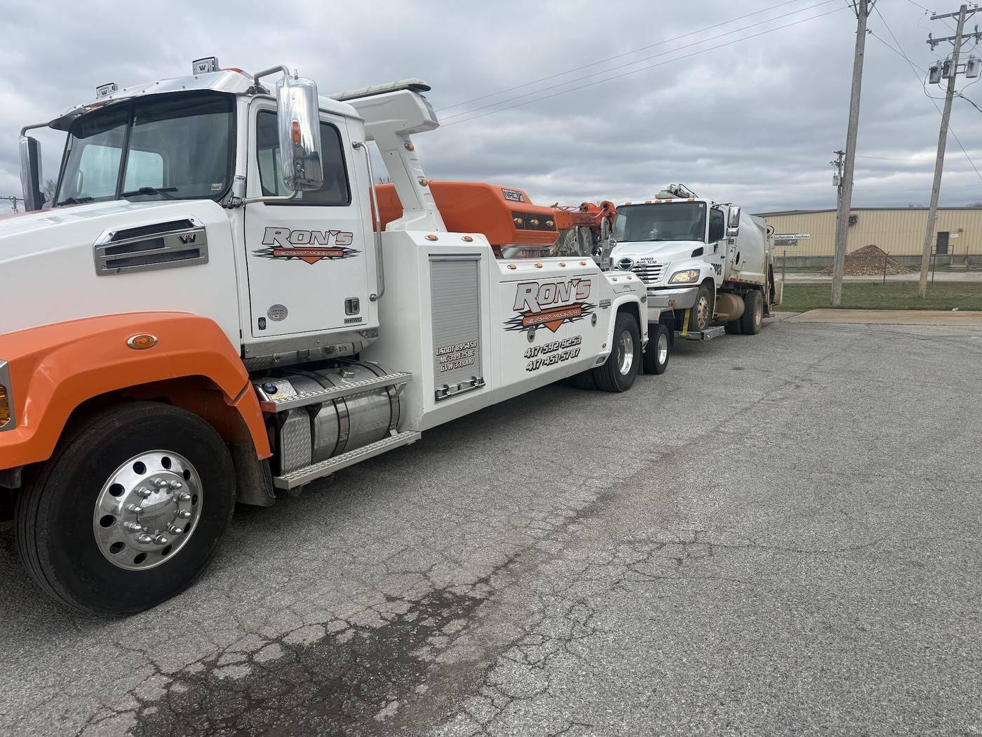 White and orange Ron's heavy wrecker towing a refuse truck