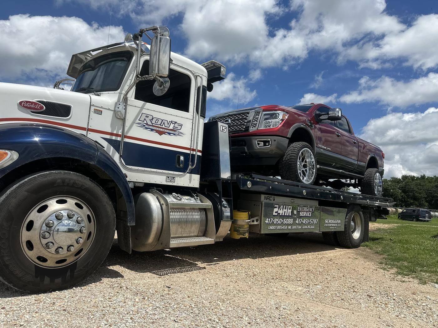 White and navy Ron's Peterbilt flatbed hauling a red pickup under a big sky
